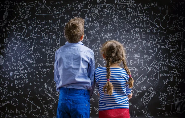 Cute little boy and girl in front of a big blackboard. — Stock Photo, Image