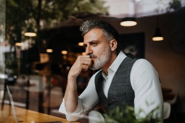 Modern ofiste oturan düşünceli olgun yöneticinin portresi..