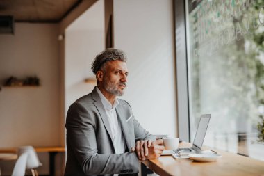 Yetişkin bir işadamı, bilgisayarını kullanarak kahve dükkanında çalışıyor..