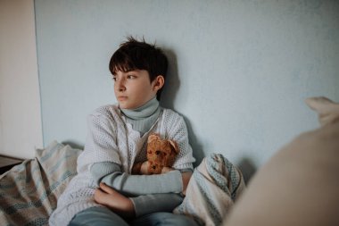 Zavallı üzgün genç kız yatak odasında oyuncak ayısını tutuyor. Yoksulluk kavramı.