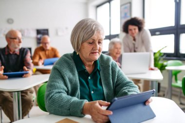 Öğretmen yardımı ile dijital beceriler öğrenen yaşlı kadın, tablet kullanıyor.