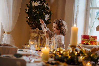 Noel 'de evde oturup Noel süslerine bakan neşeli küçük bir kızın portresi..