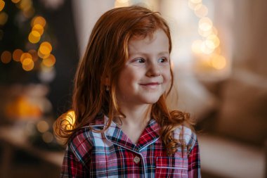 Noel 'de evde kızıl saçlı küçük bir kızın yakın plan portresi. Kameraya bakıyor..
