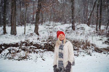Kış manzarasında kar yağışının tadını çıkaran yaşlı bir kadın. Yaşlılar için kış mevsimi.