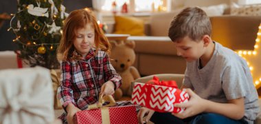 Erkek ve kız pijamalarıyla yılbaşı hediyelerini açıyorlar. Kopyalama alanı olan pankart.