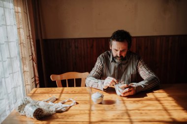 Masada oturup çay içen ümitsiz bir adamın portresi. Evin içi eski..