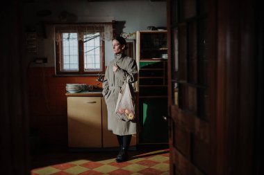 Eski kırsal mutfakta yarısı boş bir alışveriş çantasıyla duran bir kadın. Yoksulluk kavramı.