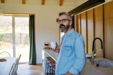 Orta yaşlı bir adam mutfakta kahve içiyor. Sabah vakti.