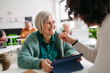 Öğretmen yardımı ile dijital beceriler öğrenen yaşlı kadın, tablet kullanıyor.