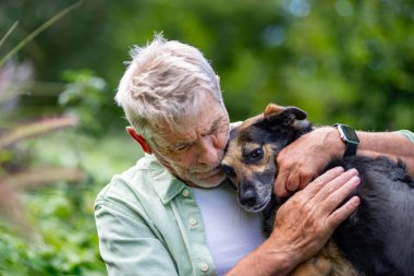 Kıdemli adam sadık köpeğini kucaklıyor, dışarıda dinleniyor.