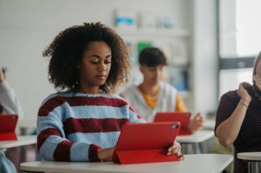 Sınıfta dikkatlice dinleyen genç öğrenci, dijital tablet kullanıyor.