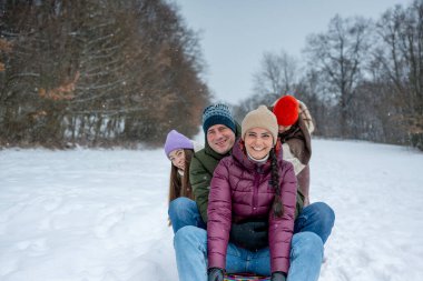 Aile, karlı tepede kış kızağı kayarken eğleniyor. Kış eğlencesi.