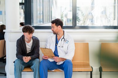 Modern hastane bekleme odasında genç bir hastayla konuşan bir doktor..