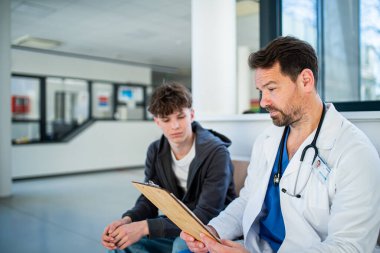 Modern hastane bekleme odasında genç bir hastayla konuşan bir doktor..