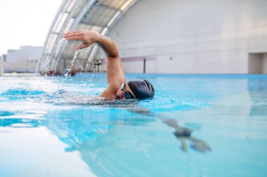 Odaklanmış yüzücü mavi suda sürünerek yüzüyor..