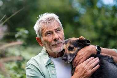 Kıdemli adam sadık köpeğini kucaklıyor, dışarıda dinleniyor.