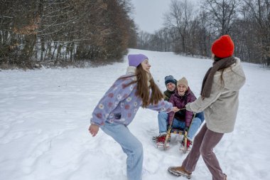 Aile, karlı tepede kış kızağı kayarken eğleniyor. Kış eğlencesi.