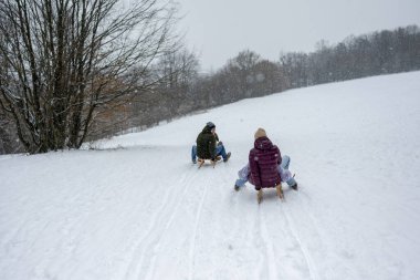 Aile, karlı tepede kış kızağı kayarken eğleniyor. Kış eğlencesi.