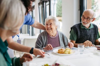 Bakıcı, huzurevinde kalan yaşlılara yemek servisi yapıyor. Huzurevi yemek odası..