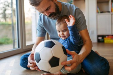 Baba yerde oğluyla top oynuyor..