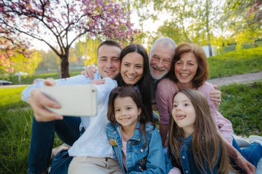 Bahar doğasında dışarıda oturup selfie çeken üç nesillik ailenin ön görüntüsü..