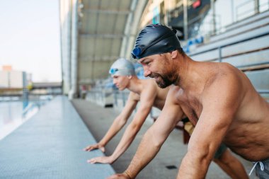Baba ve genç yüzme antrenmanına hazırlanıyor, esniyorlar. Yüzme hocası ve yüzücü..