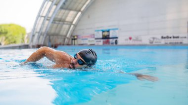 Odaklanmış yüzücü mavi suda sürünerek yüzüyor..
