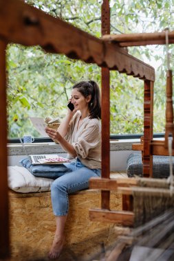 İş kadını kumaş parçalarına bakıyor, ahşap tezgahın yanında oturuyor. Döngülü tekstil, küçük kumaş dokuma işi ve dairesel ekonomi.