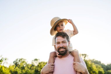 Babam sıcak yaz gününde küçük bir çocuğu omuzlarında taşıyor. Yan görünüm.