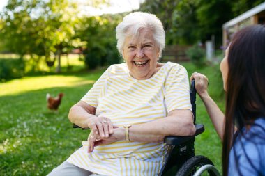 Tekerlekli sandalyede yaşlı bir hastayla yürüyen kadın hemşire..