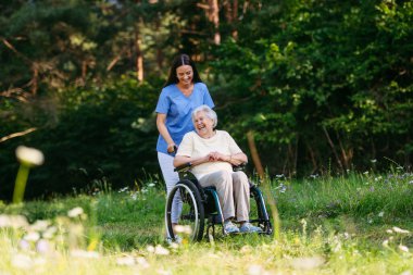 Tekerlekli sandalyedeki yaşlı bir hastayla evde yürüyen hemşire. Bahar yürüyüşü.
