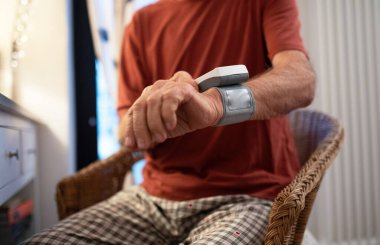 Evde bilek monitörüyle kan basıncını ölçen yaşlı bir adam..