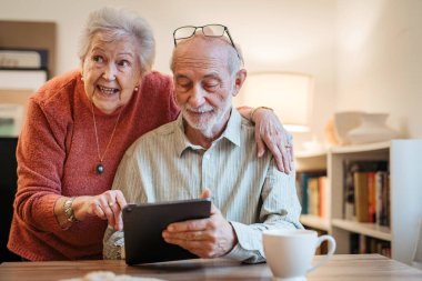 Kıdemli çift tabletle çalışıyor, rezervasyon yaptırıyor ya da internetten alışveriş yapıyor. Dijital okuryazarlık.