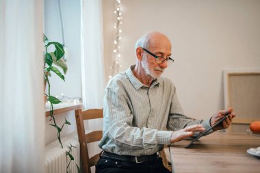 Yaşlı adam dijital tablet kullanıyor, internetten alışveriş yapıyor.