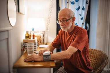 Evde bilek monitörüyle kan basıncını ölçen yaşlı bir adam..