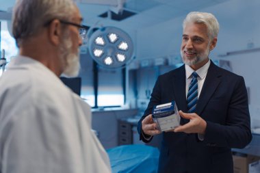 Tıbbi satış temsilcisi doktorlara yeni ilaçlar sunuyor. Muayene odasında duruyor. Hastane ayarları.