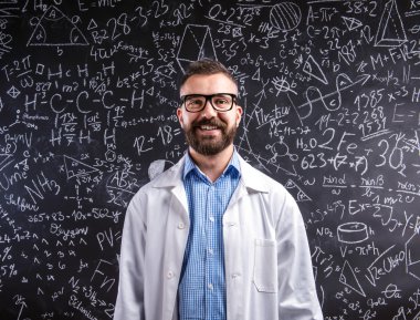 Teacher in white coat  and eyeglasses against big blackboard wit