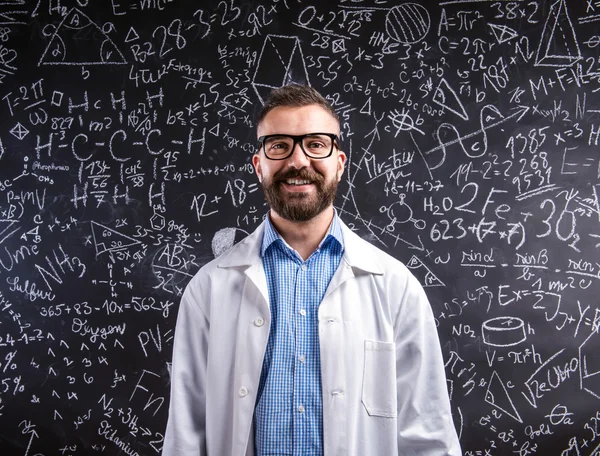 Teacher in white coat  and eyeglasses against big blackboard wit — Stock Photo, Image