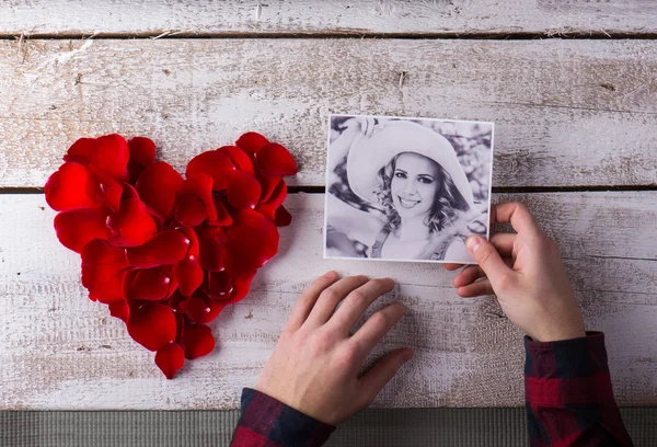 Mans si tiene per mano la foto delle sue amiche. Cuore di petalo di rosa rossa . — Foto Stock