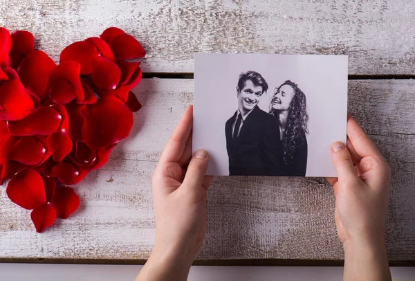 Un uomo con in mano la sua foto e quella delle sue ragazze. Cuore di petalo di rosa . — Foto Stock