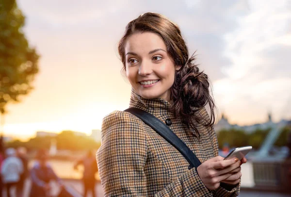 Woman in brown coat with smart phone in sunny park — Φωτογραφία Αρχείου