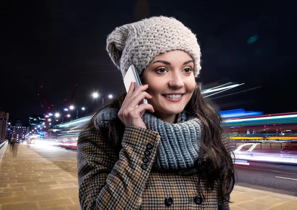 Woman in winter coat with smart phone in night city — Stockfoto