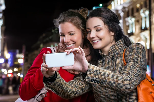 Two women taking selfie with smart phone in night city — Stok fotoğraf