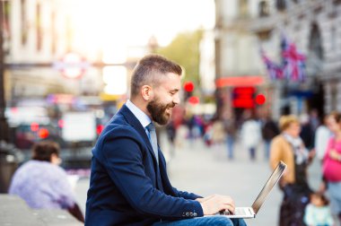Hipster manager working on laptop on sunny Piccadilly Circus, Lo