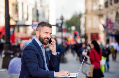 Manager with laptop and smart phone, sunny Piccadilly Circus, Lo