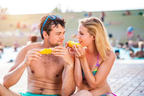 Pareja en trajes de baño en la piscina comiendo maíz — Foto de Stock