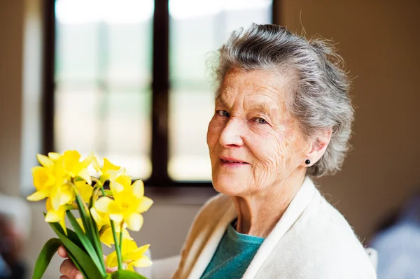 Femme âgée près de la fenêtre tenant bouquet de jonquilles — Photo