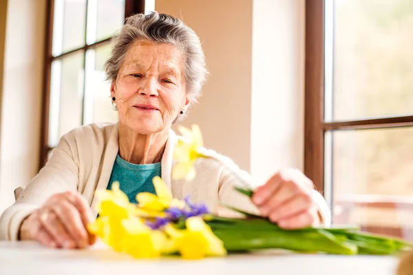 Mulher sênior pela janela organizando buquê de narcisos — Fotografia de Stock