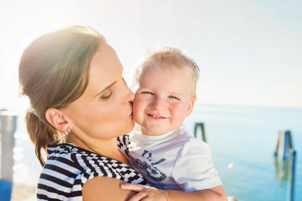 Mother kissing her boy, sunny summer by the water — Zdjęcie stockowe