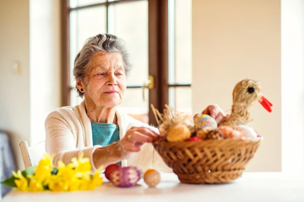 Senior woman arranging basket with Easter eggs and daffodils — Stock Photo, Image